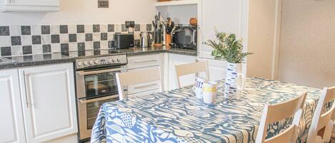 A kitchen with white cabinets, a stove, and a microwave. There is a table with a blue tablecloth and chairs.