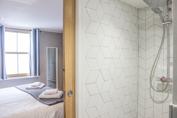 A hotel room with a bed, a shower, and a window with curtains.