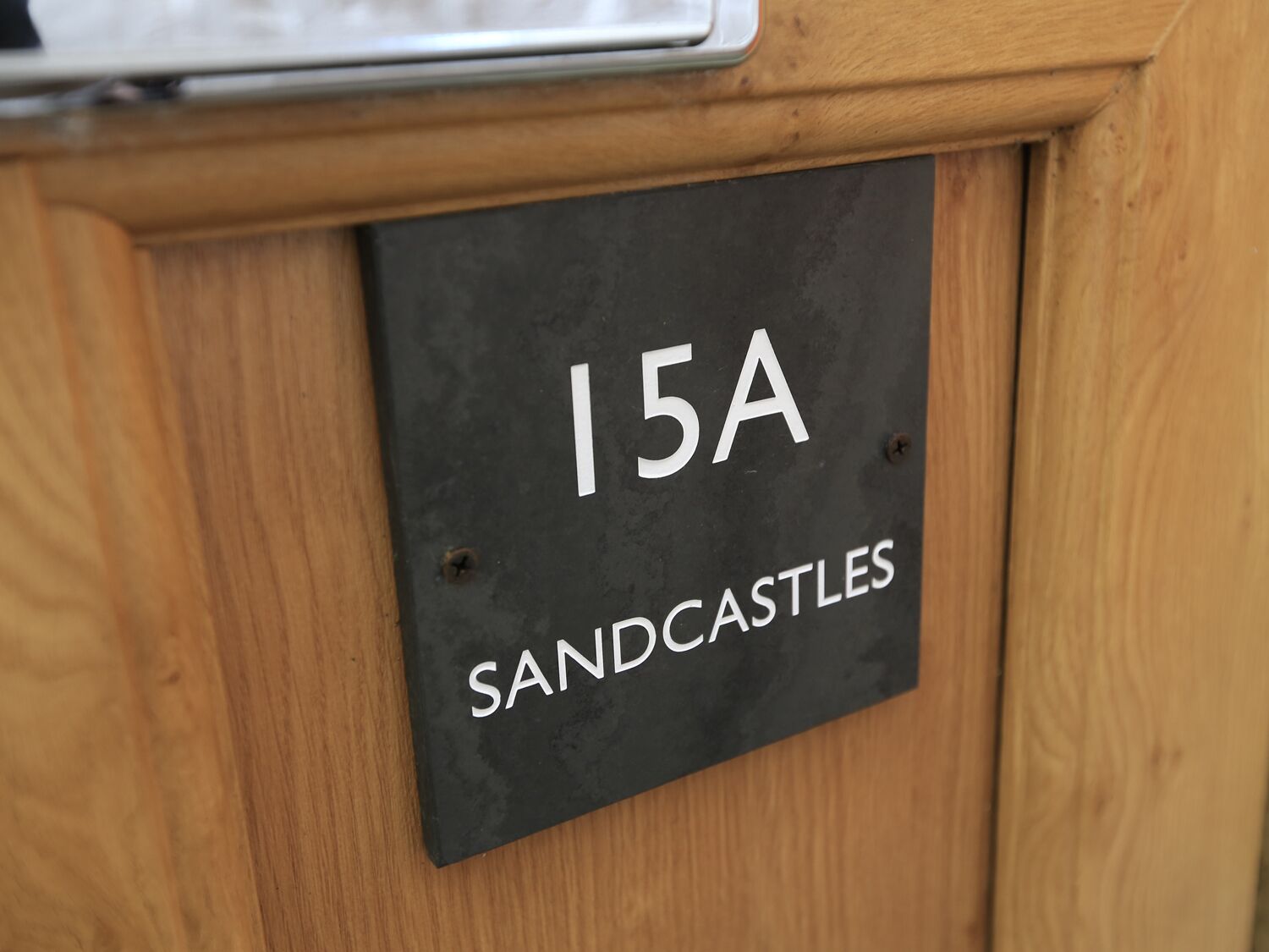 Una señal con el número 15A y el texto 'Sandcastles' sobre un fondo oscuro, montada sobre una superficie de madera.
