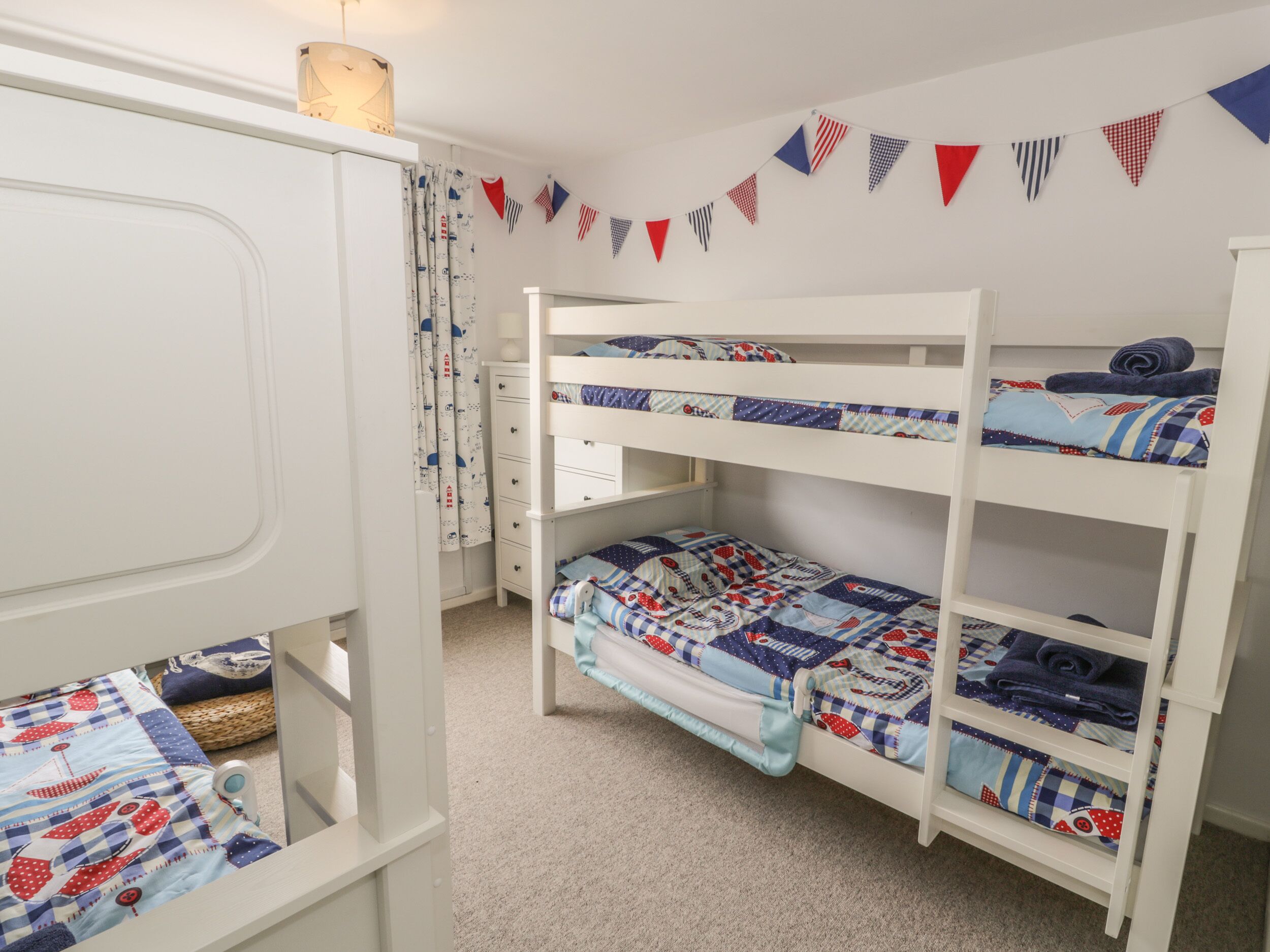 A children's bunk bed room with a white door, a small desk, and a wall decorated with bunting.