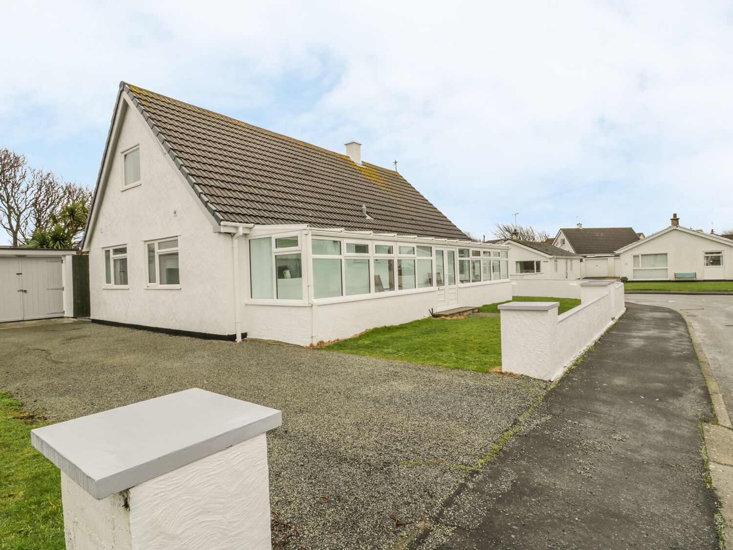 A single-story house with a sloped roof, a conservatory with glass walls, and a gravel driveway.