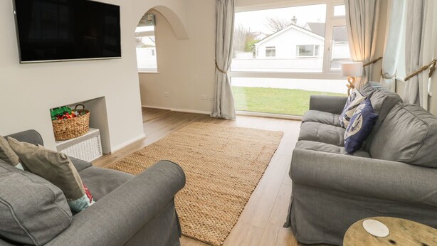 Ein Wohnzimmer mit zwei grauen Sofas, einem Flachbildfernseher, einem gewebten Teppich und einem Fenster mit Vorhängen.