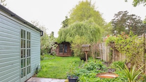 A garden with a wooden cabin, a shed, and a variety of plants. - 3 Station Cottages (Wymondham)
