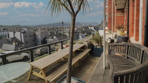 A balcony with wooden benches, a small palm tree, and potted plants. - Beaulieu House (Llandudno)