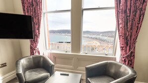 A room with two leather armchairs, a small table, and a TV mounted on the wall. - Beaulieu House (Llandudno)