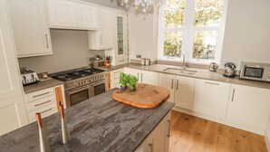 A modern kitchen with white cabinets, a wooden countertop, a stove, and a window with a view of greenery. - Beaulieu House (Llandudno)
