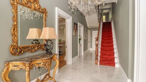 A grand hallway with a marble floor, a red carpeted staircase, a large ornate mirror, and a chandelier. - Beaulieu House (Llandudno)