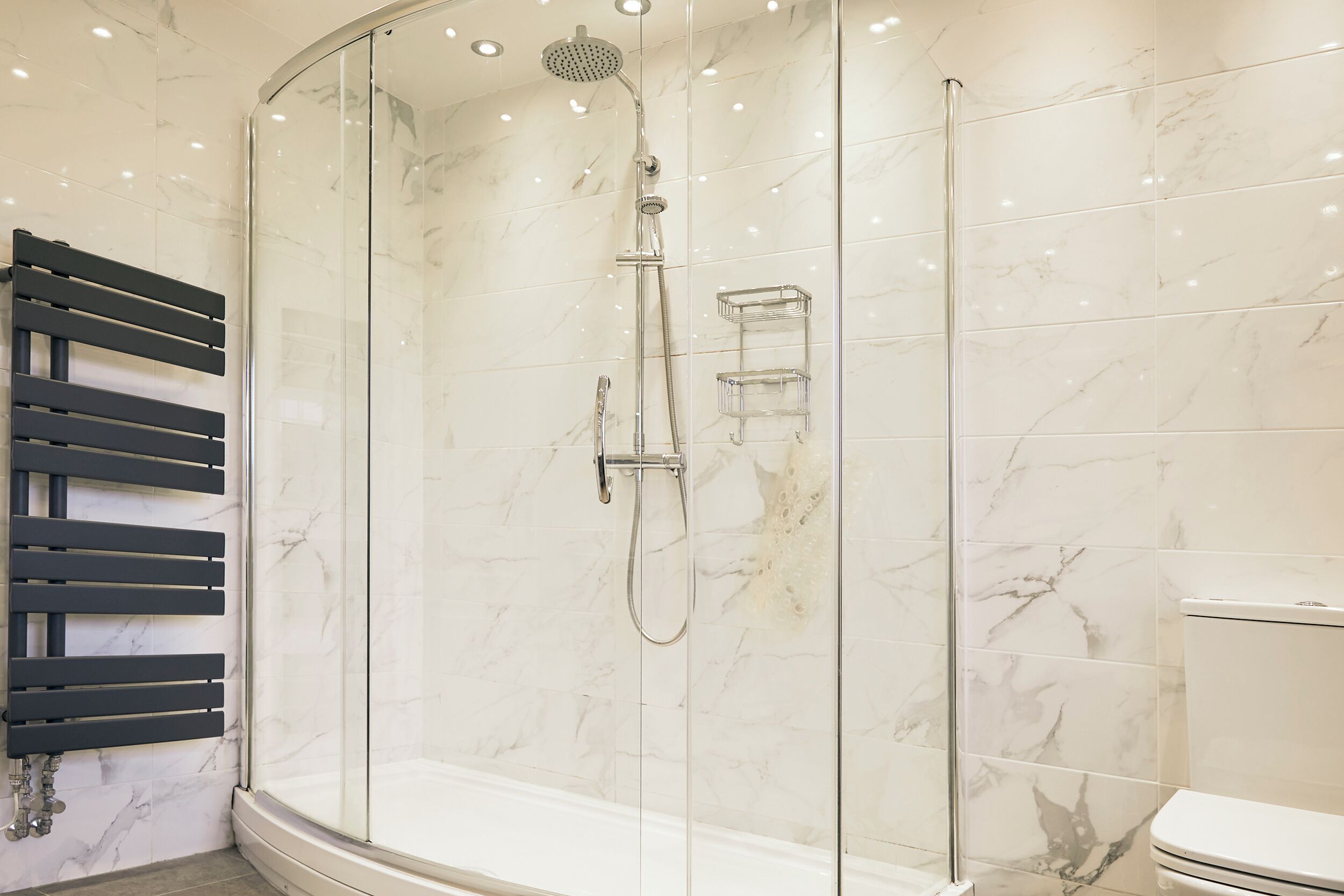 Une salle de bain moderne avec une douche à parois de verre, un porte-serviettes noir et des toilettes blanches.