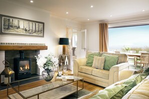 A living room with a fireplace, sofa, and a dining area with a view.