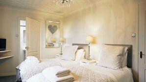 Ein Hotelzimmer mit zwei Betten, einem Fernseher auf einem Regal, einem Spiegel mit Herzverzierung und einer Kristallleuchter.