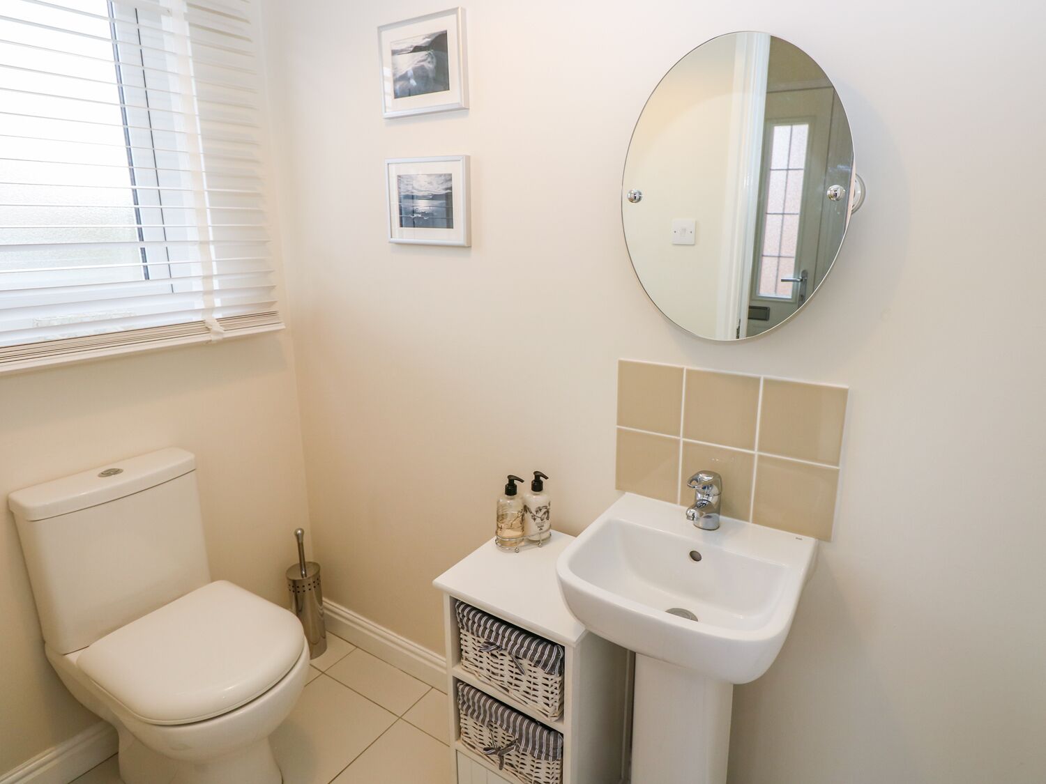 A bathroom with a toilet, a sink, and a mirror. There are two framed pictures on the wall.