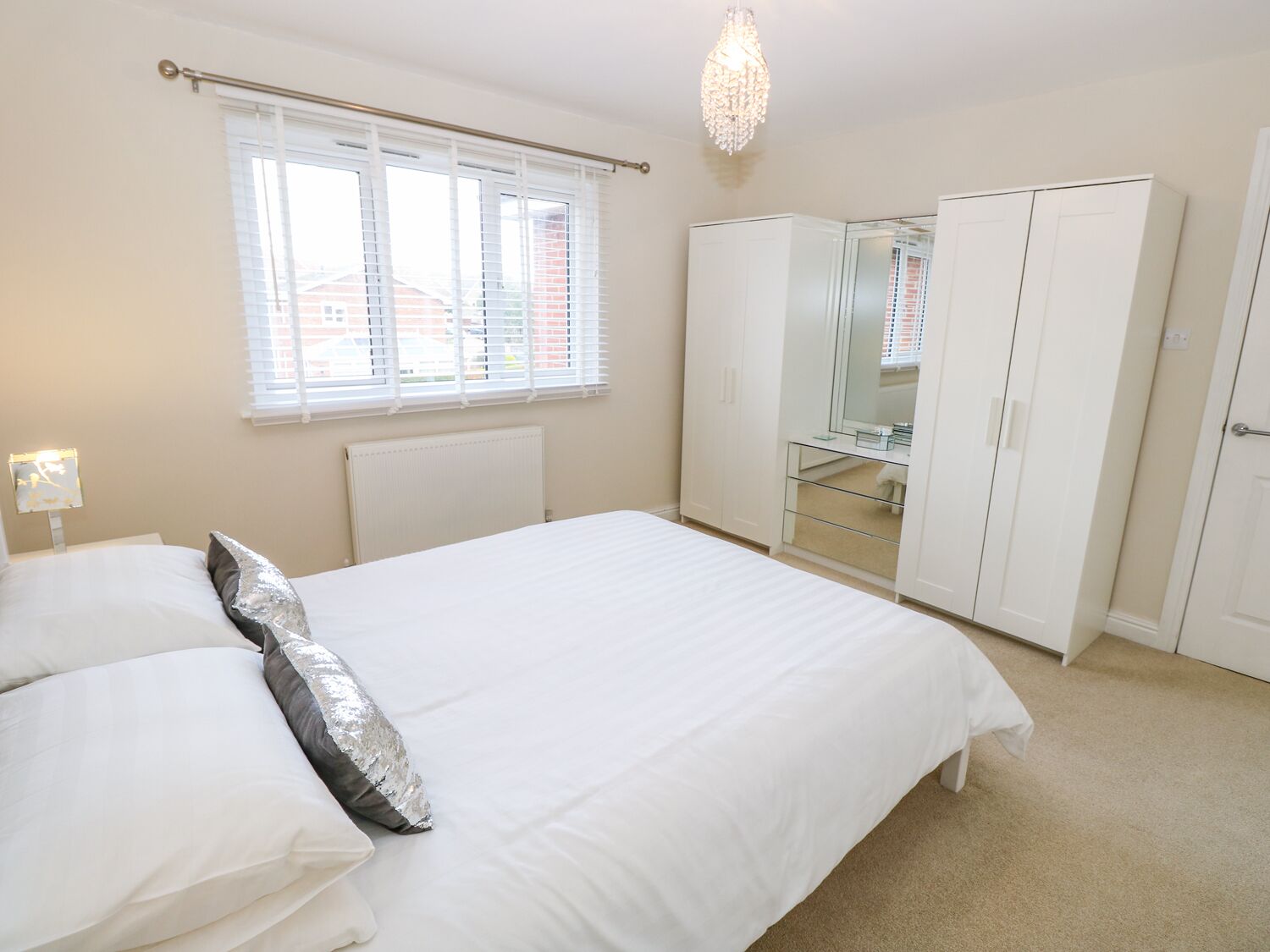 A bedroom with a bed, a wardrobe, a mirror, and a chandelier.