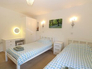 A bedroom with two beds, a bedside table, a mirror, and a wall-mounted light fixture.