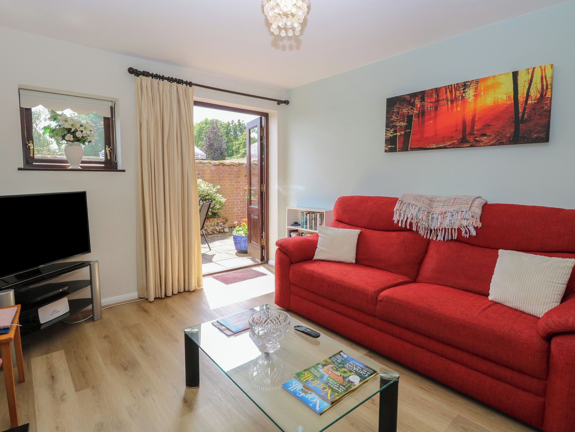 A living room with a red sofa, a flat-screen TV, a glass coffee table, and a painting on the wall.