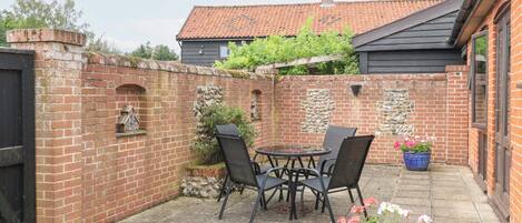A patio area with a brick wall, a stone wall with a small archway, a round table with chairs, and a potted plant.