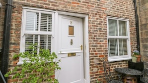 A brick house with a white door and two windows, a small garden, and outdoor furniture.