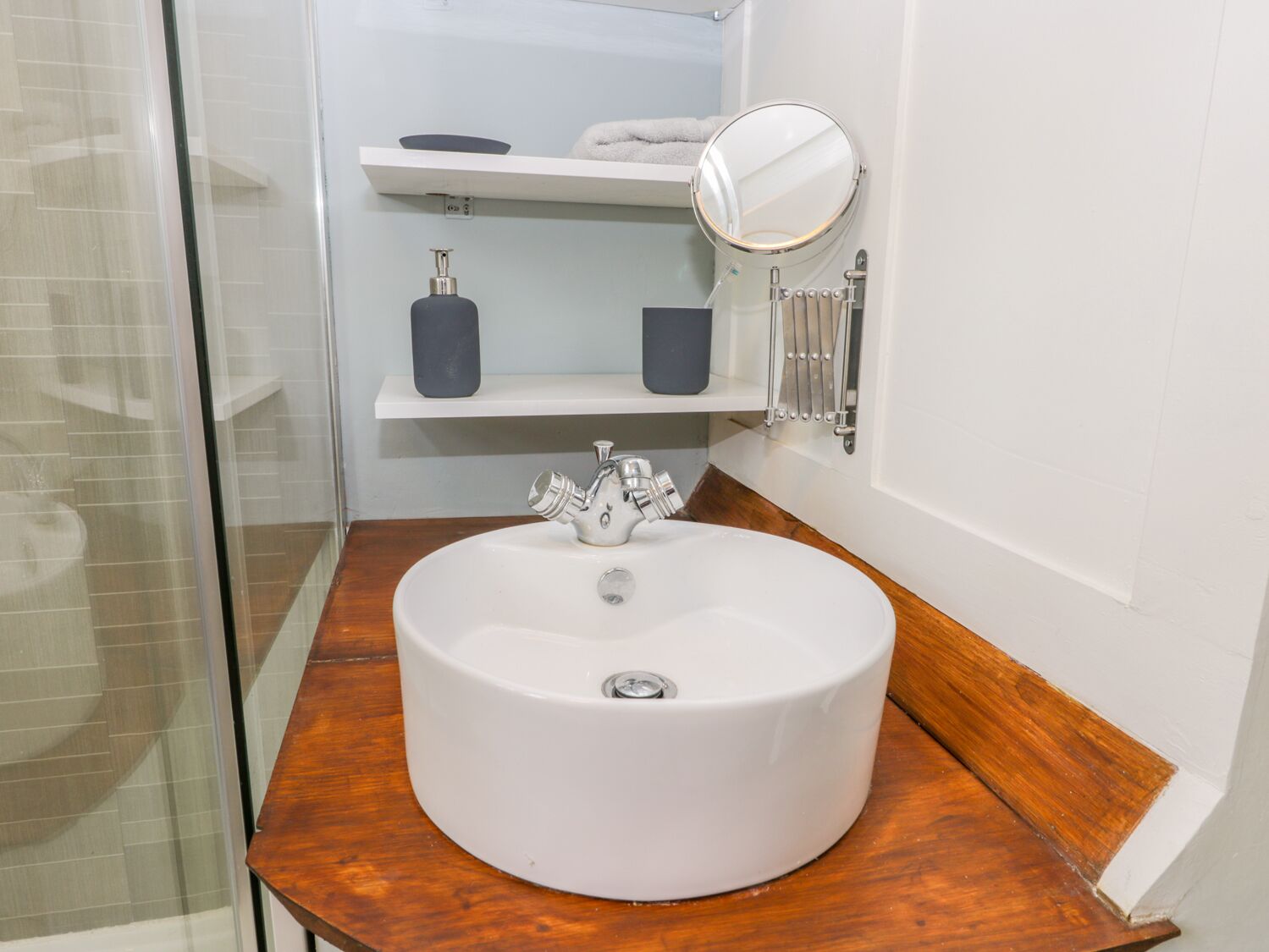Une salle de bain avec un lavabo blanc, un miroir et deux étagères contenant des articles de toilette.