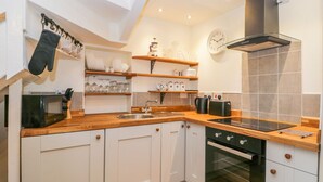 A modern kitchen with white cabinets, wooden countertops, a built-in oven, a microwave, and a hanging pot rack.