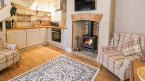A cozy living room with a fireplace, a kitchen with white cabinets, and a plaid sofa.