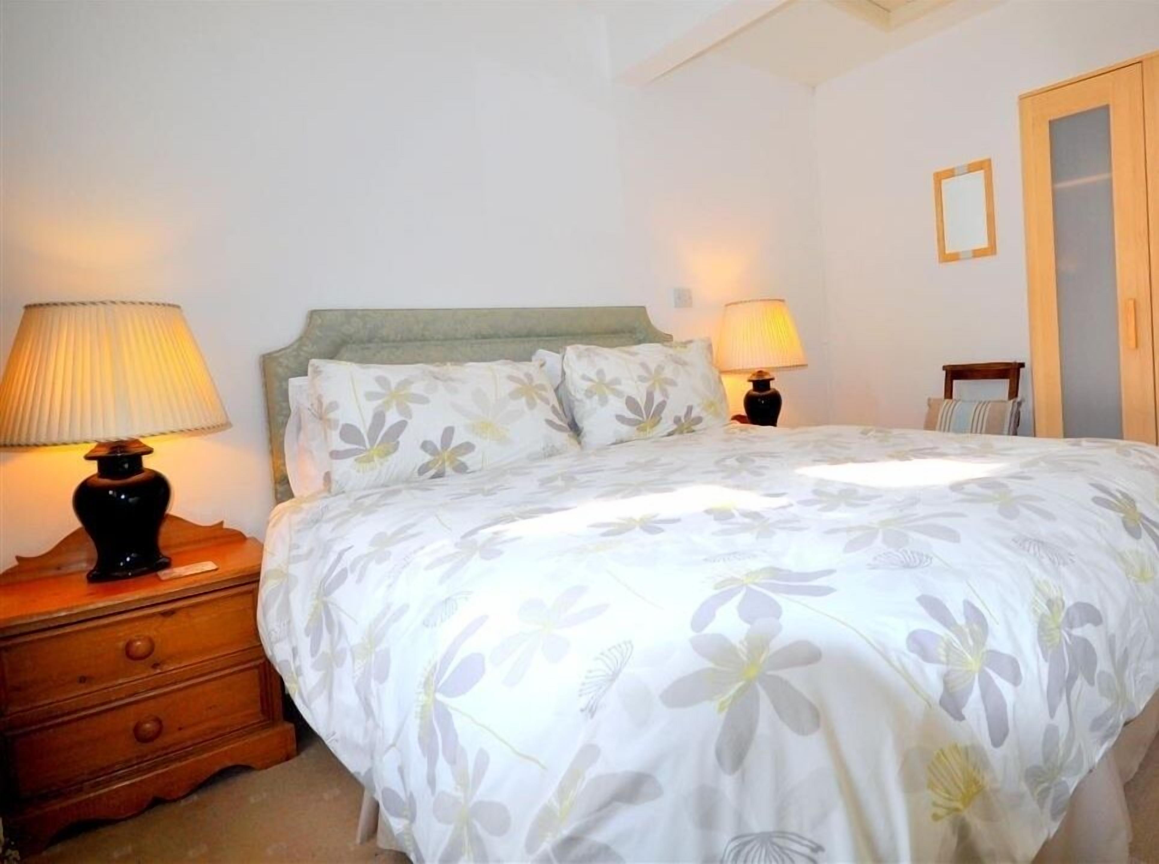 Une chambre à coucher comprenant un lit, deux lampes de chevet, une table de chevet en bois, une commode et une armoire.