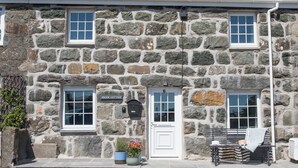 Une petite maison en pierre avec une porte blanche, deux fenêtres et une boîte aux lettres.