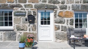 Un bâtiment en pierre avec une porte blanche portant le numéro 6, une boîte aux lettres et deux pots de fleurs.