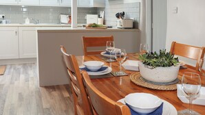 Une cuisine moderne avec des meubles blancs, une table à manger en bois dressée pour deux personnes et une plante en pot posée sur la table.