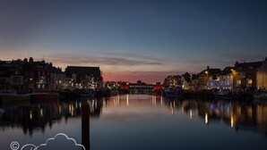 Een waterlandschap in de schemering, met rustig water dat gebouwen en boten weerspiegelt.