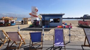 Een strandzicht met een klein kioskje, strandstoelen en een redershut.