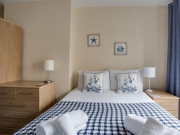 A hotel room with a bed, two bedside tables, a wooden dresser, and a wall with two framed pictures.