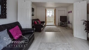 A spacious living room with a black leather sofa, a television, and a chandelier. - Ocean Swell (Weymouth)
