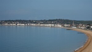 A coastal view with a sandy beach and a row of buildings along the shore. - Ocean Swell (Weymouth)