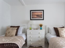 Un dormitorio con dos camas, una mesita de noche con cajones, una lámpara y un cuadro en la pared.