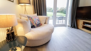 A modern living room with a sofa, a lamp, a television, and a sliding glass door leading to a garden. - Gwelfor (Cemaes Bay)