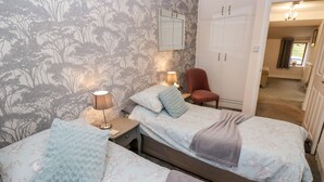 Une chambre avec deux lits, une armoire, une chaise et une table de chevet avec une lampe.