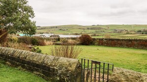 Un paysage rural avec un mur de pierres, un champ herbeux et des collines à l’horizon.