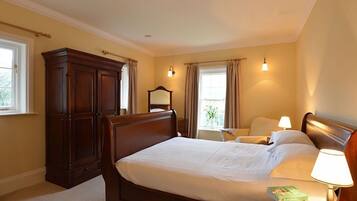 A bedroom with a large wooden bed, a nightstand with a lamp, a wardrobe, and two windows with curtains.