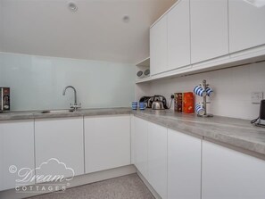 A modern kitchen with white cabinets, a stainless steel sink, and a countertop with kitchen appliances and storage containers.