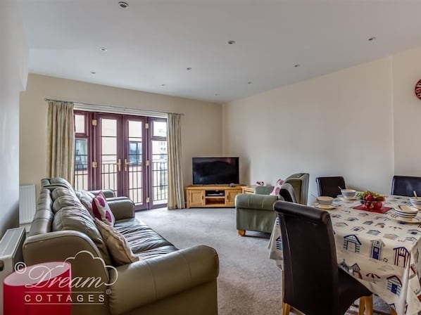 A living room with a sofa, a TV, a dining table with chairs, and a window with curtains.