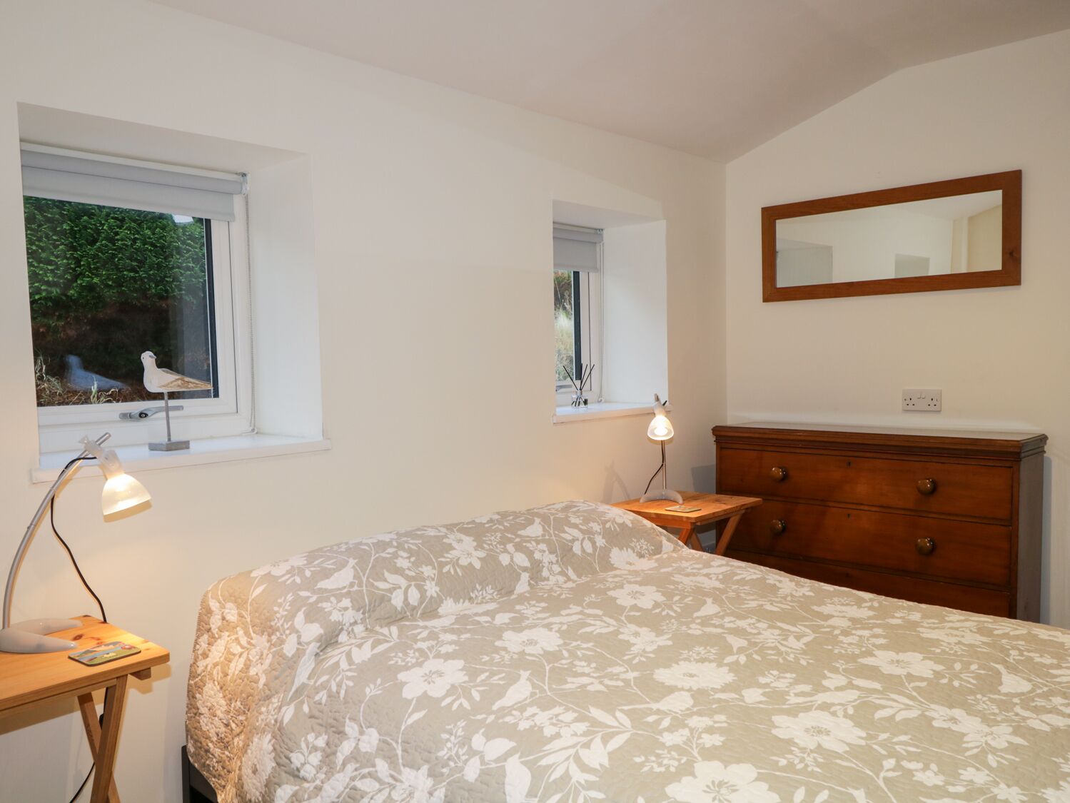 Ein Schlafzimmer mit einem Bett, zwei Nachttischen, einer Holzkommode und zwei Fenstern mit Jalousien.