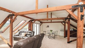 Ein Dachzimmer mit freiliegenden Holzbalken, einem Ledersofa, einem Esstisch mit Stühlen und Blick durch Dachfenster.