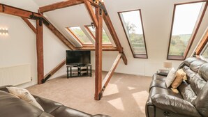 Ein geräumiges Schlafzimmer im Loft-Stil mit hohen Decken, freiliegenden Holzbalken, Dachfenstern, einem großen Fenster, einem Flachbildfernseher und einem Ledersofa.