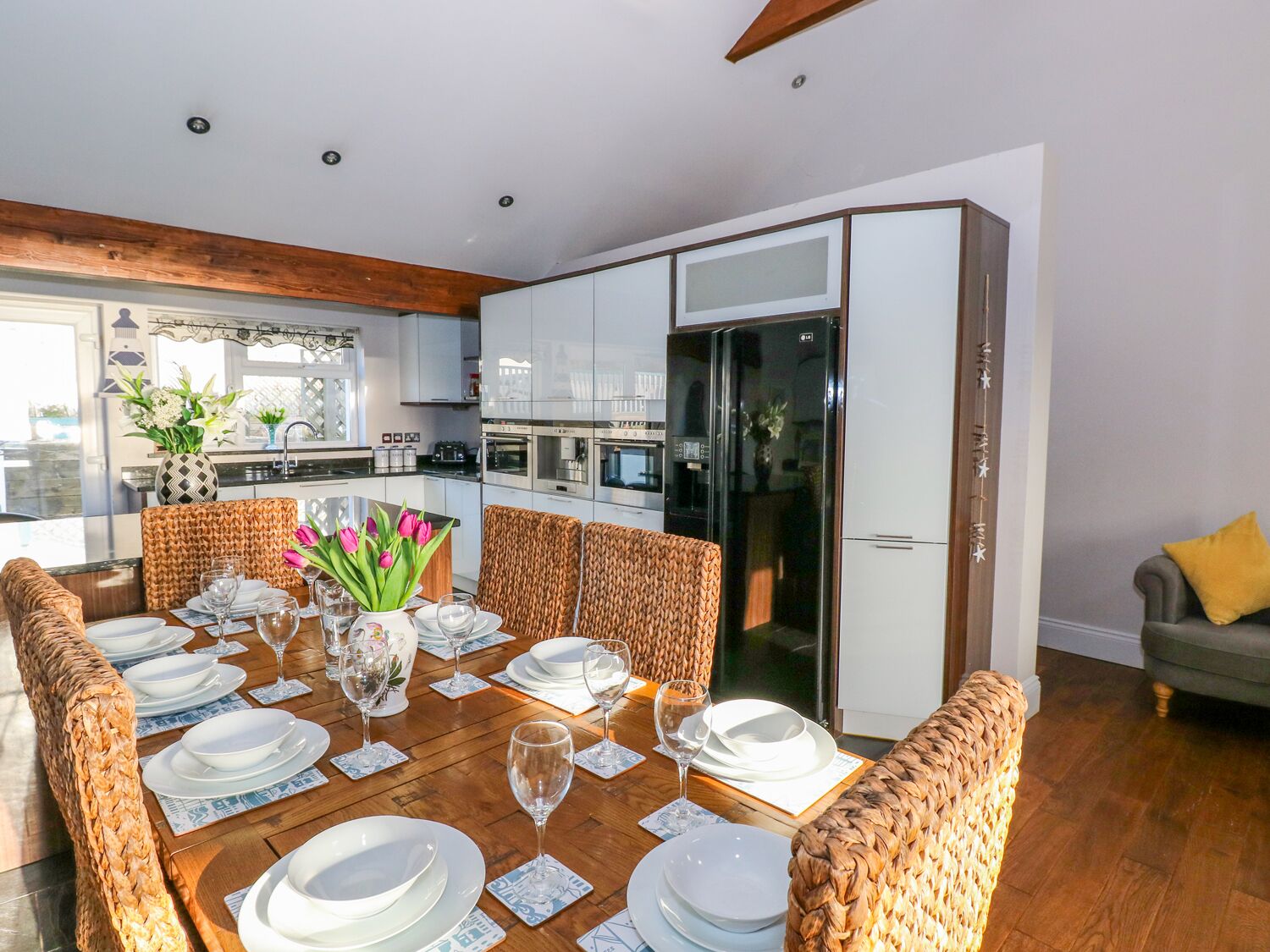 A modern kitchen with white cabinets, a black refrigerator, and a dining area with wicker chairs and a wooden table set for six.