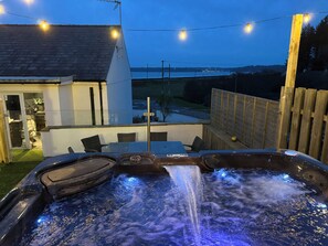 Un jacuzzi con caída de agua, rodeado por una terraza con sillas y luces colgantes.
