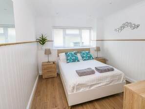 Une chambre à coucher comprenant un lit, deux tables de chevet, une fenêtre avec des stores, une plante en pot et un élément de décoration murale.