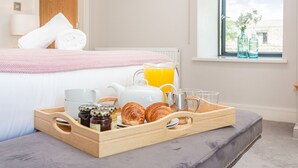 Ein ordentlich gedecktes Frühstücksbrett mit Croissants, einem Teekessel, Tassen und einem Glas Orangensaft auf einem grauen Pouf im Hotelzimmer.