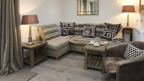 Ein gemütliches Wohnzimmer mit einer Eckcouch, zwei Beistelltischen mit Lampen, einem Couchtisch und einer gemusterten Decke.