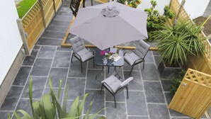 Eine Terrasse mit Tisch, vier Stühlen, einem großen Sonnenschirm und Kübelpflanzen.