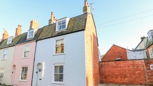 A row of terraced houses with distinct pastel colors, a brick wall, and a paved street. - Lobster Cottage (Weymouth)