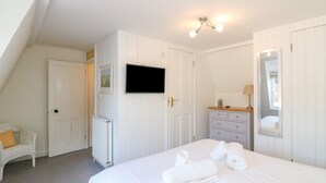 A bedroom with a bed, a dresser, a TV, a radiator, and a white chair. - Lobster Cottage (Weymouth)